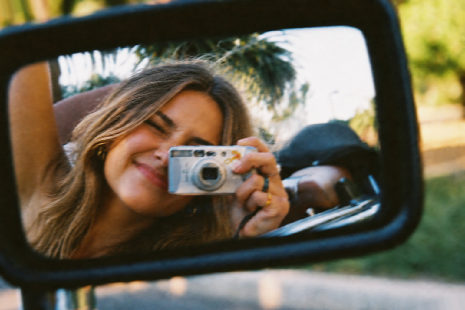 Reflection in a car mirror of a woman photographing with a compact camera — Livis camera hire Brisbane